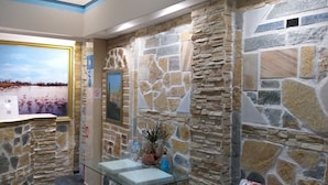 A lobby with stone walls, a reception desk, a framed painting, and a potted plant. - Petrakis Beach (Corfu)