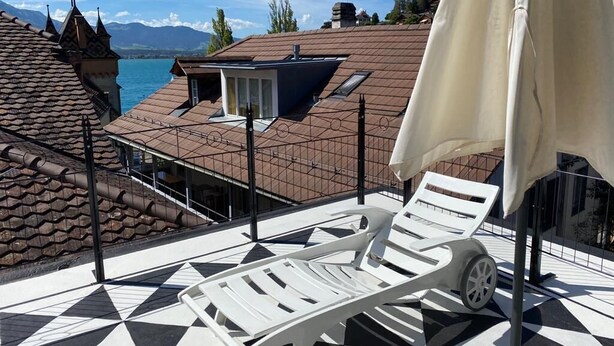 Une terrasse dotée d’un sol carrelé à motifs géométriques, d’un fauteuil de jardin blanc et d’un parasol blanc.