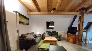 A living room with a wooden ceiling, a black leather sofa, a wooden coffee table, and a television on a wooden cabinet. - Yellow house: secluded location, sauna hut, terrace, fenced - vacation with dog (Bodendorf)