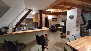 A cozy kitchen with wooden beams, a dining area with a wooden table, and a living room with a sofa and a fireplace. - Yellow house: secluded location, sauna hut, terrace, fenced - vacation with dog (Bodendorf)