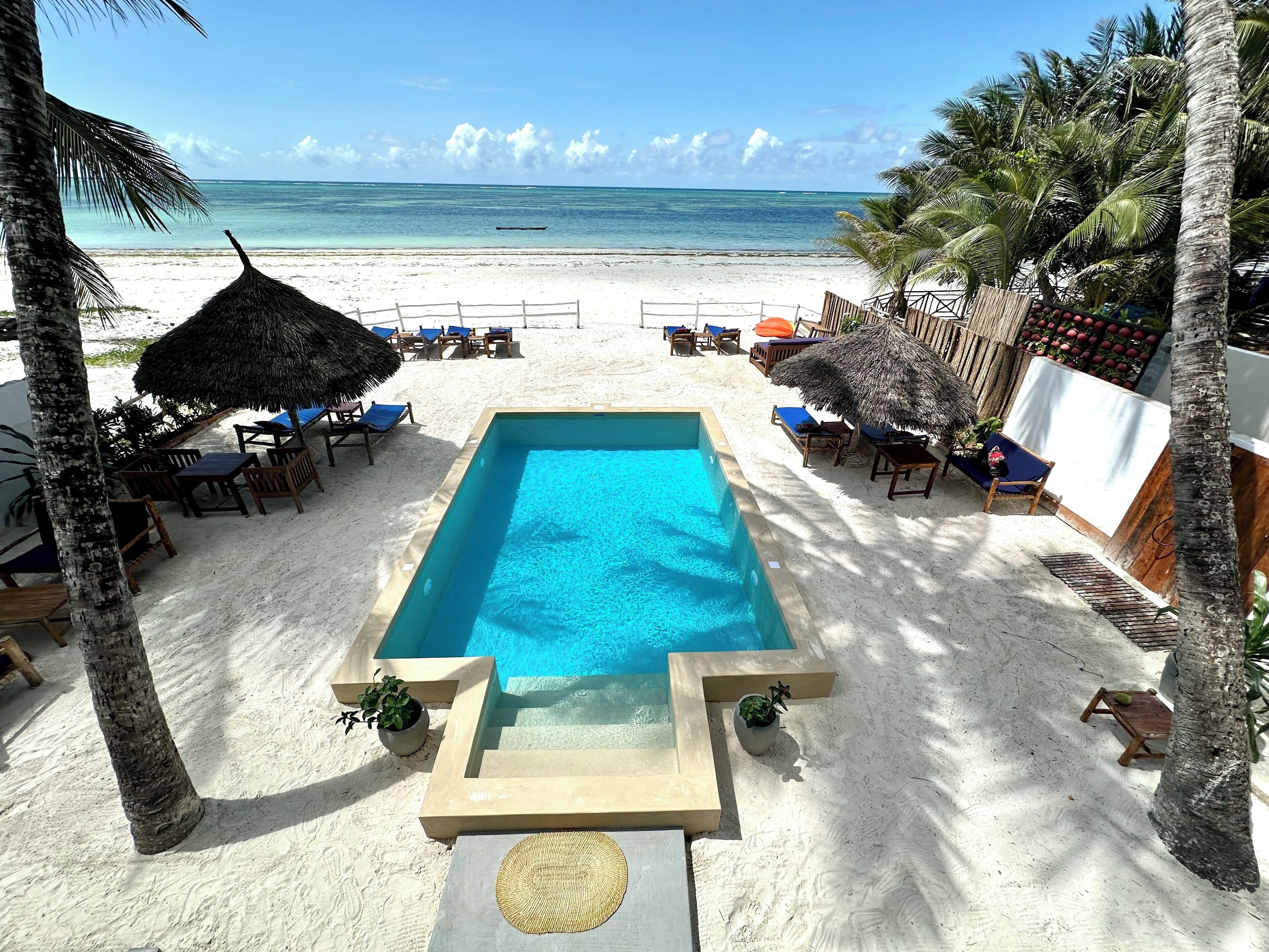 Une piscine rectangulaire à l’eau d’un bleu limpide, entourée de sable blanc.