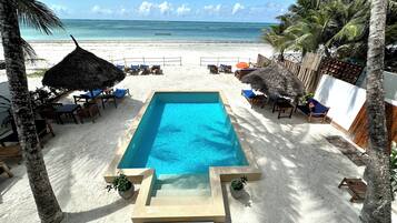 Une piscine rectangulaire à l’eau d’un bleu limpide, entourée de sable blanc.