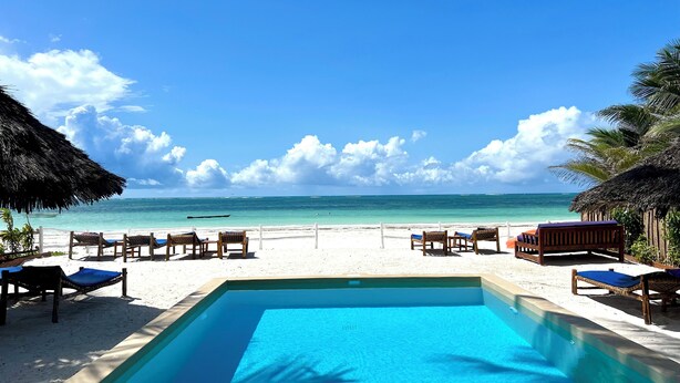 Vista de la piscina con agua cristalina, sillas de playa y una estructura de techo de paja.