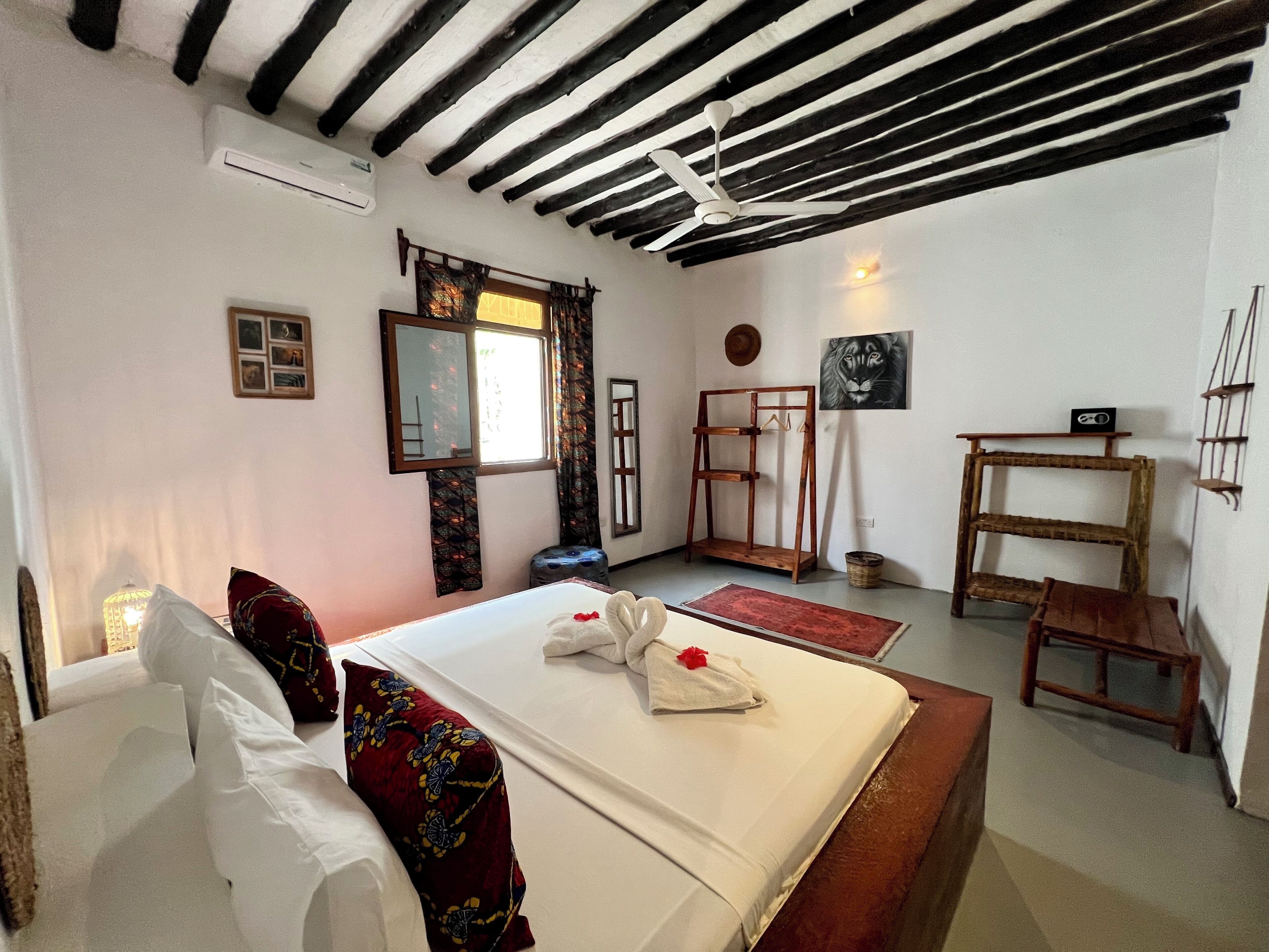 A bedroom with a bed, a wooden bench, a hanging chair, a mirror, a window with curtains, a wall-mounted shelf, and a ceiling fan.