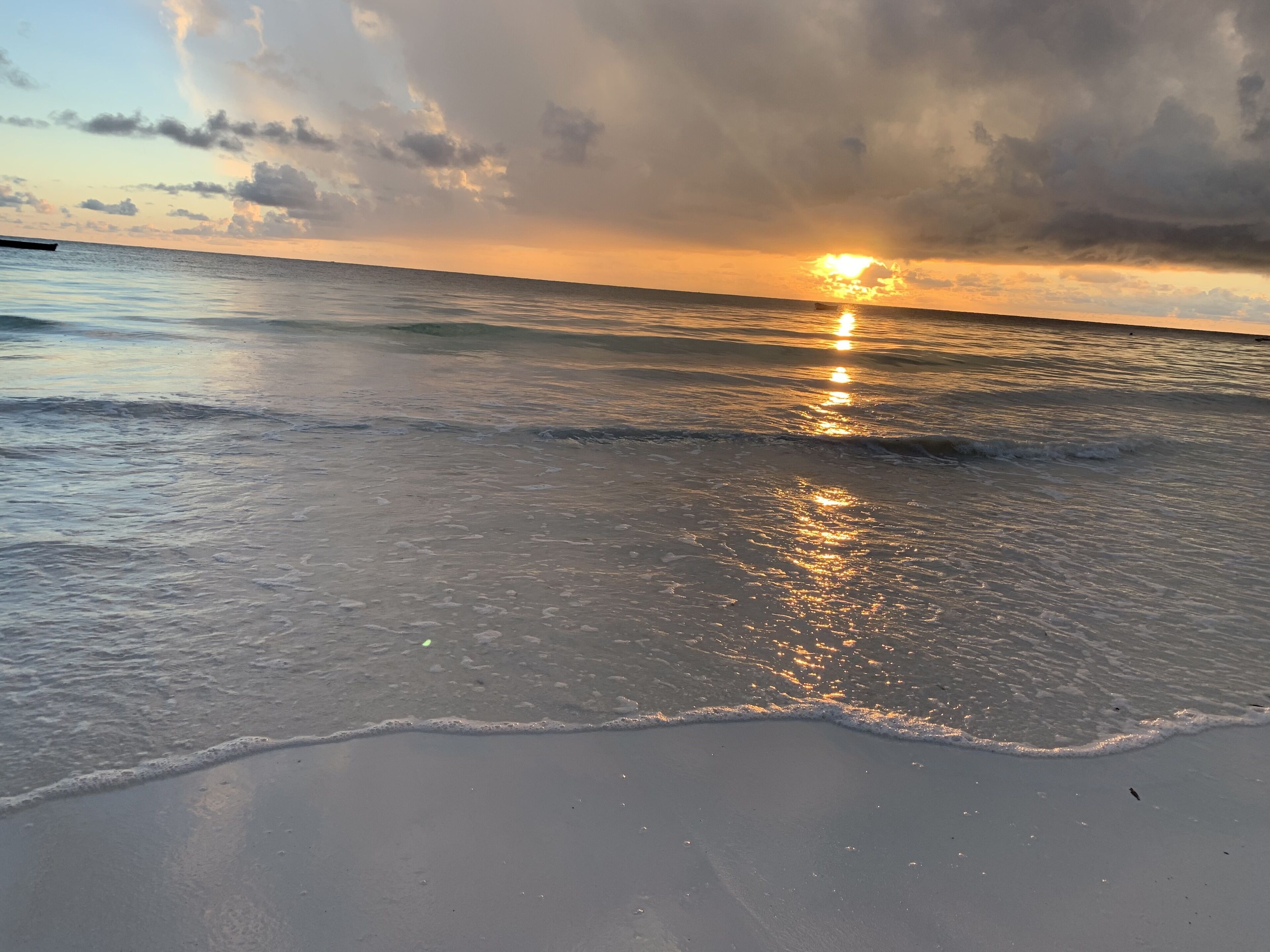 A beach with waves gently lapping at the shore and the sun setting in the distance.