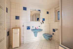 Un baño con paredes de azulejos blancos, un lavamanos azul, un inodoro y un armario.