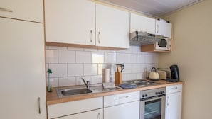 A compact kitchen with white cabinets, a microwave, a toaster, and a stove. - Awad's Yellow Apartment (Rust)