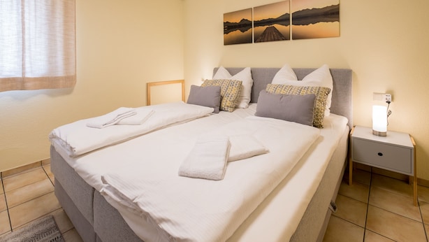A neatly made double bed with pillows and towels, a bedside table with a lamp, and a wall with three landscape paintings. - Awad's Yellow Apartment (Rust)