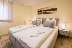 A neatly made double bed with pillows and towels, a bedside table with a lamp, and a wall with three landscape paintings. - Awad's Yellow Apartment (Rust)