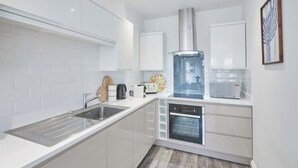 A modern kitchen with white cabinets, a stainless steel sink, a built-in oven, and a wooden floor. - Host & Stay | Number 2 at Pannett Apartments (Whitby)