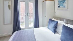 A bedroom with a bed, curtains, a wardrobe, and a window with a view of buildings. - Host & Stay | Number 2 at Pannett Apartments (Whitby)