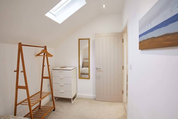 A bedroom with a wooden hanger rack, a dresser, a mirror, and a door.