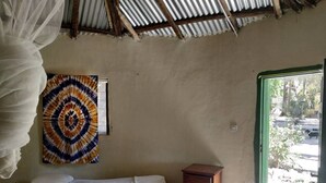 Una stanza con un letto, un comodino in legno, un arazzo colorato e vista all'esterno tramite una porta.