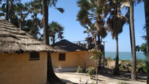 Un edificio rustico con tetto di paglia, circondato da palme e una vista limpida sull'oceano.
