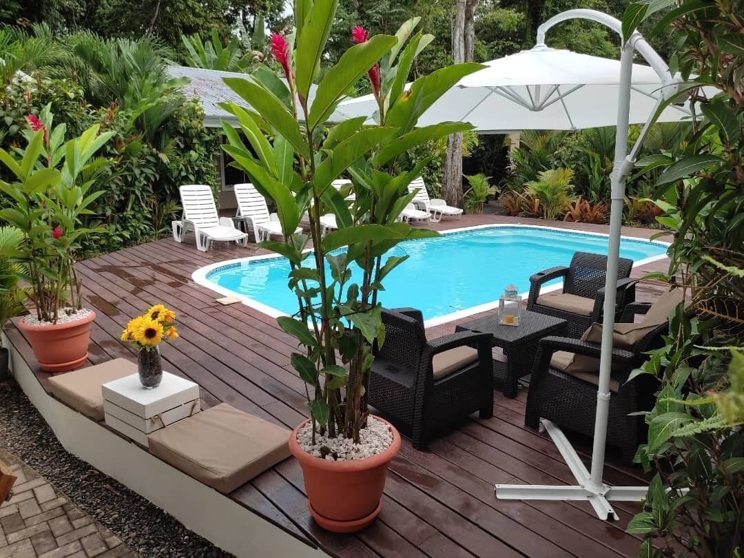 A poolside area with a wooden deck, lounge chairs, and potted plants.