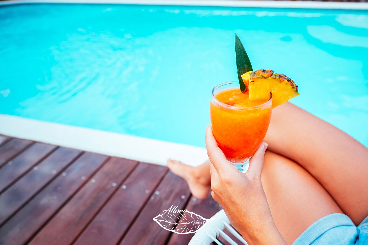 Eine Person hält an einem Pool ein tropisches Getränk.