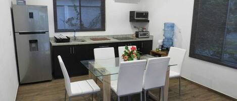 A compact kitchen with a refrigerator, microwave, and water dispenser. There is a dining table with chairs and a window with a view.