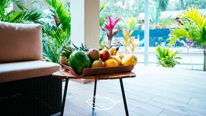A wicker sofa, a wooden table with a fruit bowl, and a tiled patio with tropical plants. - Alloro Jungle Villas (Cahuita)