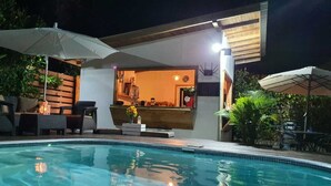 A swimming pool area with lounge chairs, umbrellas, and a bar area with a counter and seating. - Alloro Jungle Villas (Cahuita)