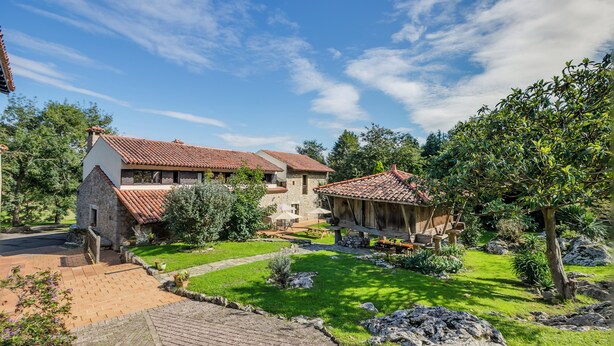 Ein traditionelles Steinhaus mit rotem Ziegeldach, einem Steinschacht und einem Garten mit einer Holzpergola.