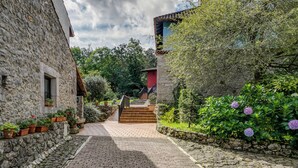 Ein Steinhaus mit roter Tür, einem Ziegelweg und einer Treppe, die zu einer höheren Ebene führt.