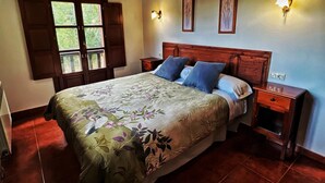 Ein Schlafzimmer mit einem hölzernen Bett, zwei Nachttischen, einem Fenster mit Rollläden und Wandleuchten.