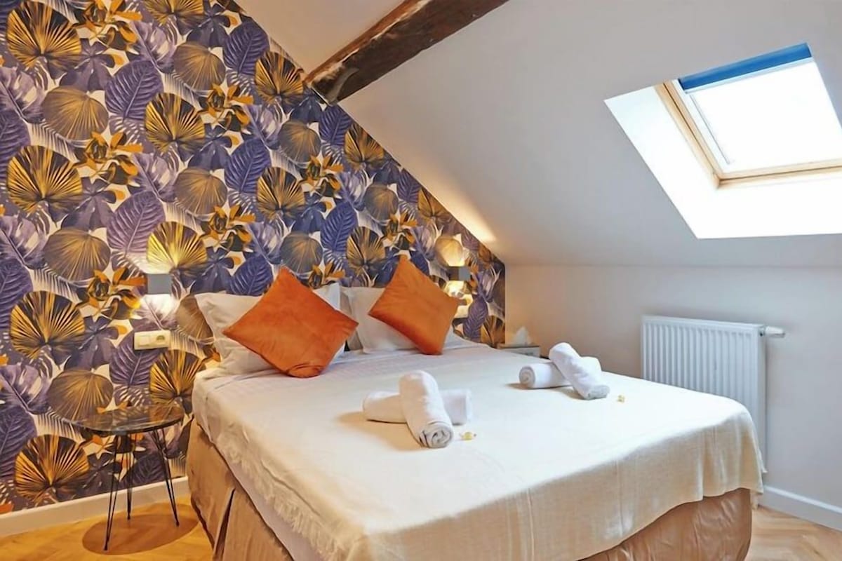 A bedroom with a sloped ceiling, a bed with pillows, a small table, and a radiator.