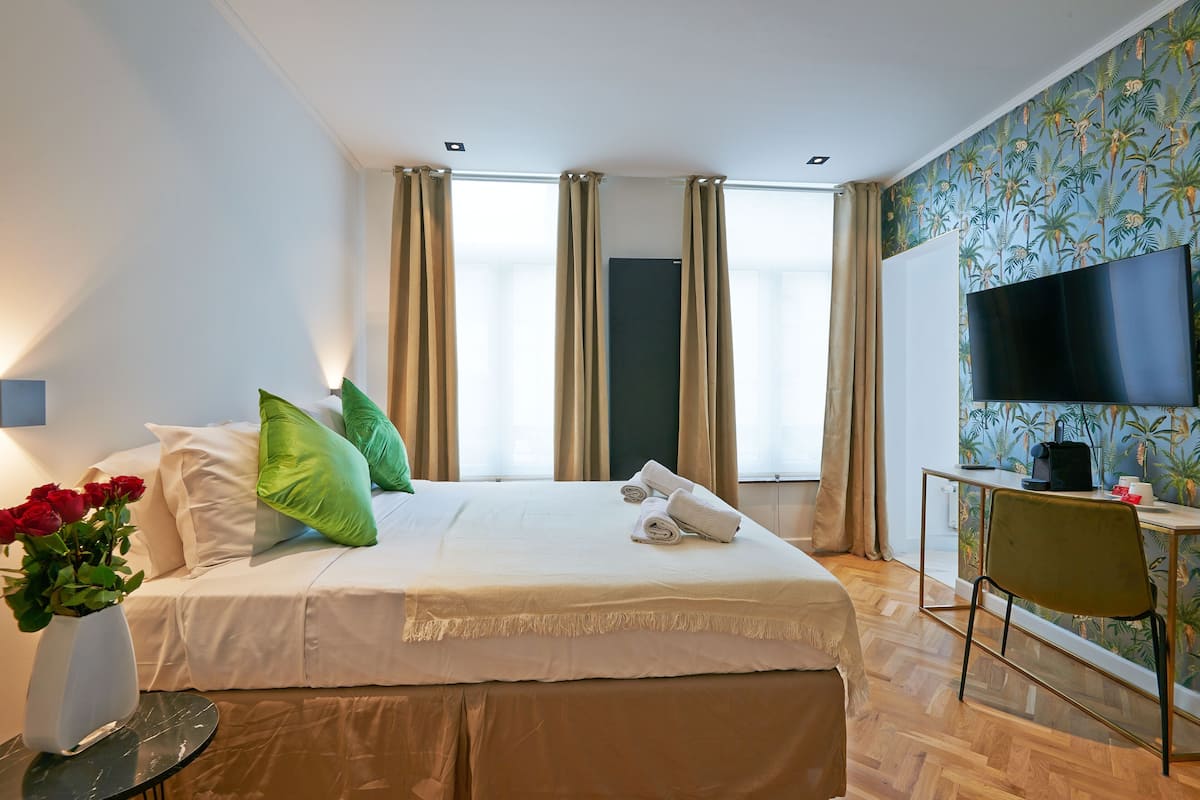 A hotel room with a bed, a desk with a chair, a TV, and a window with curtains.