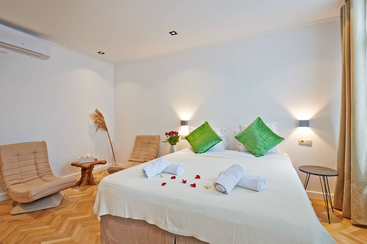 A hotel room with a large bed, two chairs, a small table, and a wall-mounted lamp.