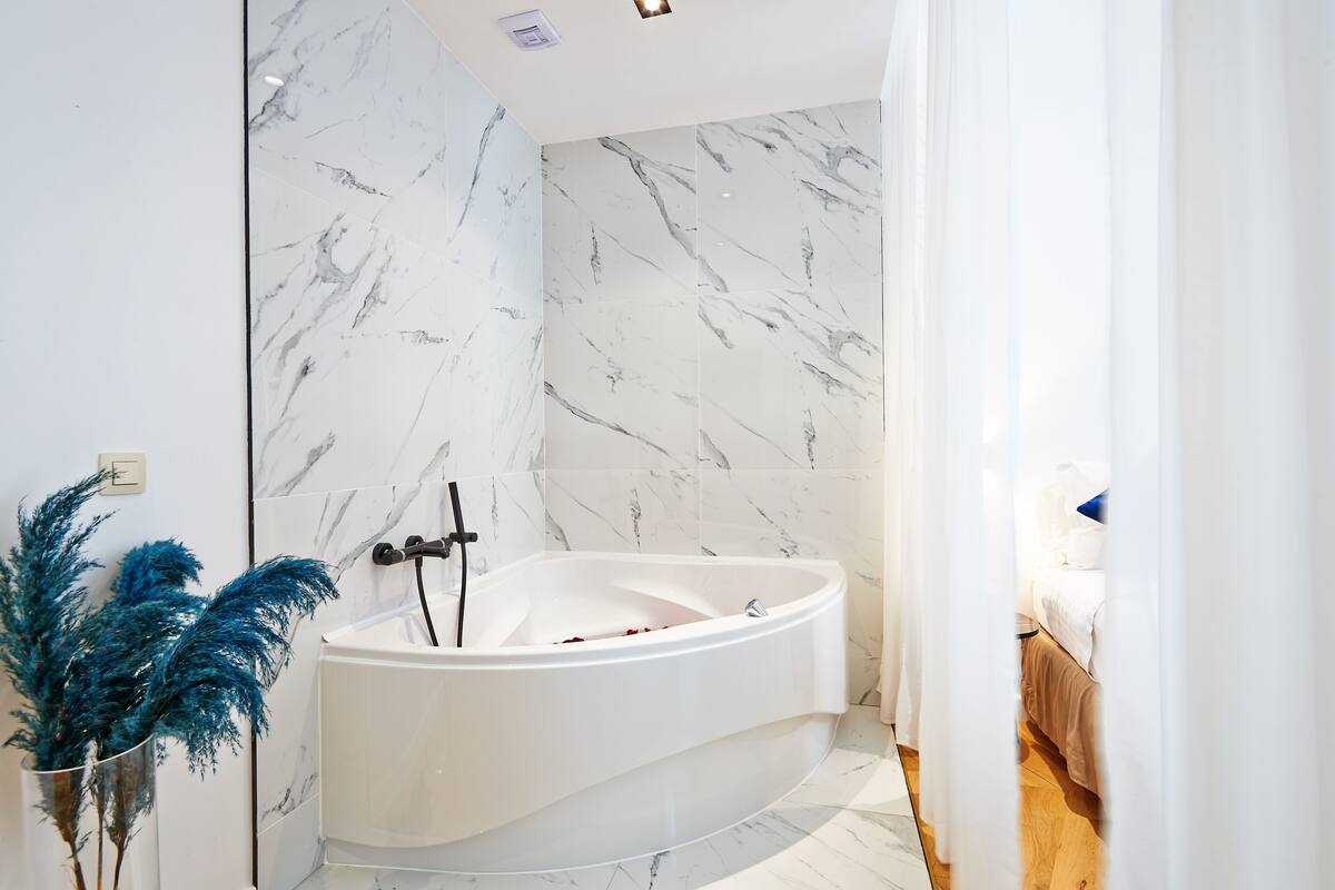 A modern bathroom with a freestanding bathtub, marble walls, and a wooden floor.