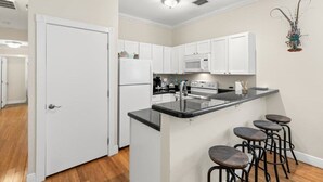 A modern kitchen with white cabinets, a black countertop, and a bar stool area. - Mesa House Dos - One block from Duval St (Key West)