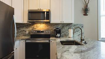 A modern kitchen with stainless steel appliances, a marble countertop, and a built-in oven.