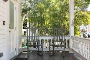 Een veranda met twee schommelstoelen, een witte balustrade en weelderige begroeiing op de achtergrond.