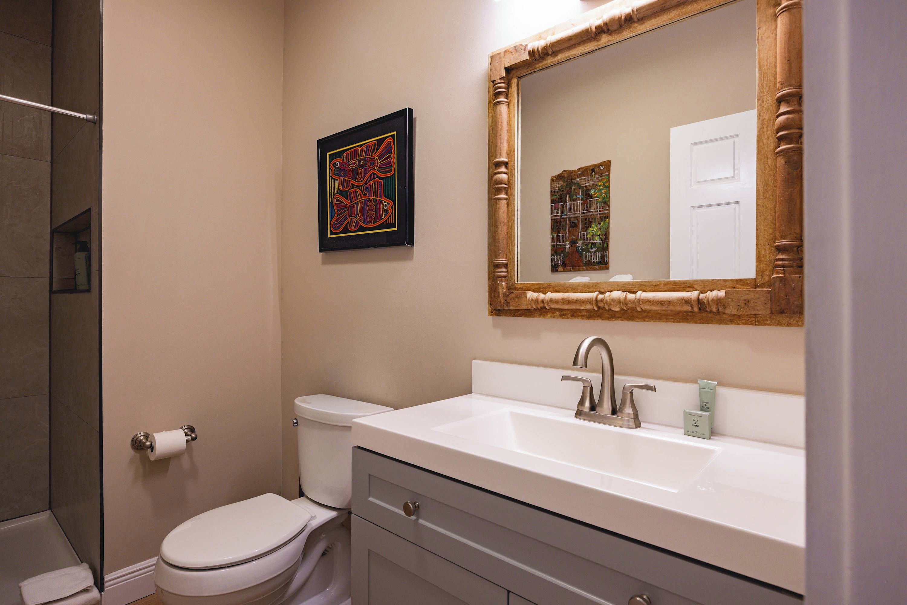 A bathroom with a toilet, a sink with a mirror, and a framed artwork on the wall.