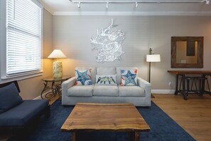 A living room with a grey sofa, decorative pillows, a wooden coffee table, a wall-mounted dragon sculpture, and a mirror on the wall. - Mesa House Dos - One block from Duval St (Key West)
