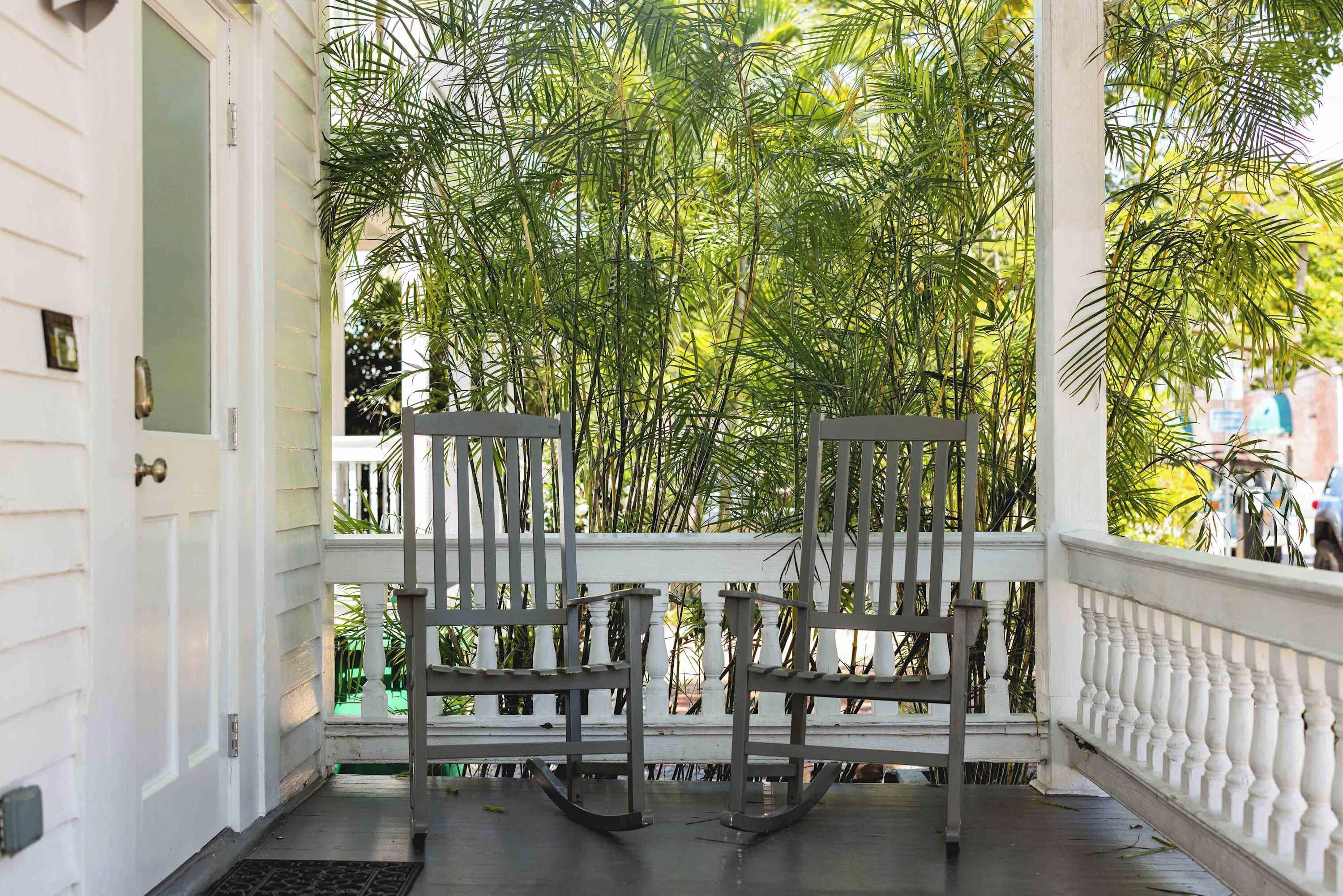 A porch with two rocking chairs, white balustrade, and dense foliage in the background.