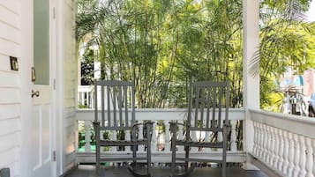 A porch with two rocking chairs, white balustrade, and dense foliage in the background.