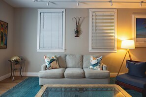 Een woonkamer met een grijze bank, twee decoratieve kussens, een blauw vloerkleed en een vloerlamp.