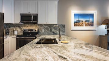 A kitchen with white cabinets, a stainless steel microwave, a stove, and a sink with a marble countertop.