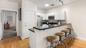A modern kitchen with white cabinets, a central island with stools, a microwave, and a stove. - Mesa House Uno - One block from Duval St (Key West)