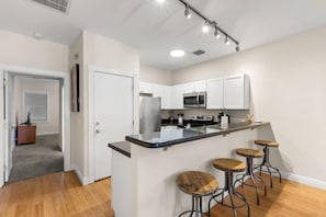 A modern kitchen with white cabinets, a central island with stools, a microwave, and a stove.