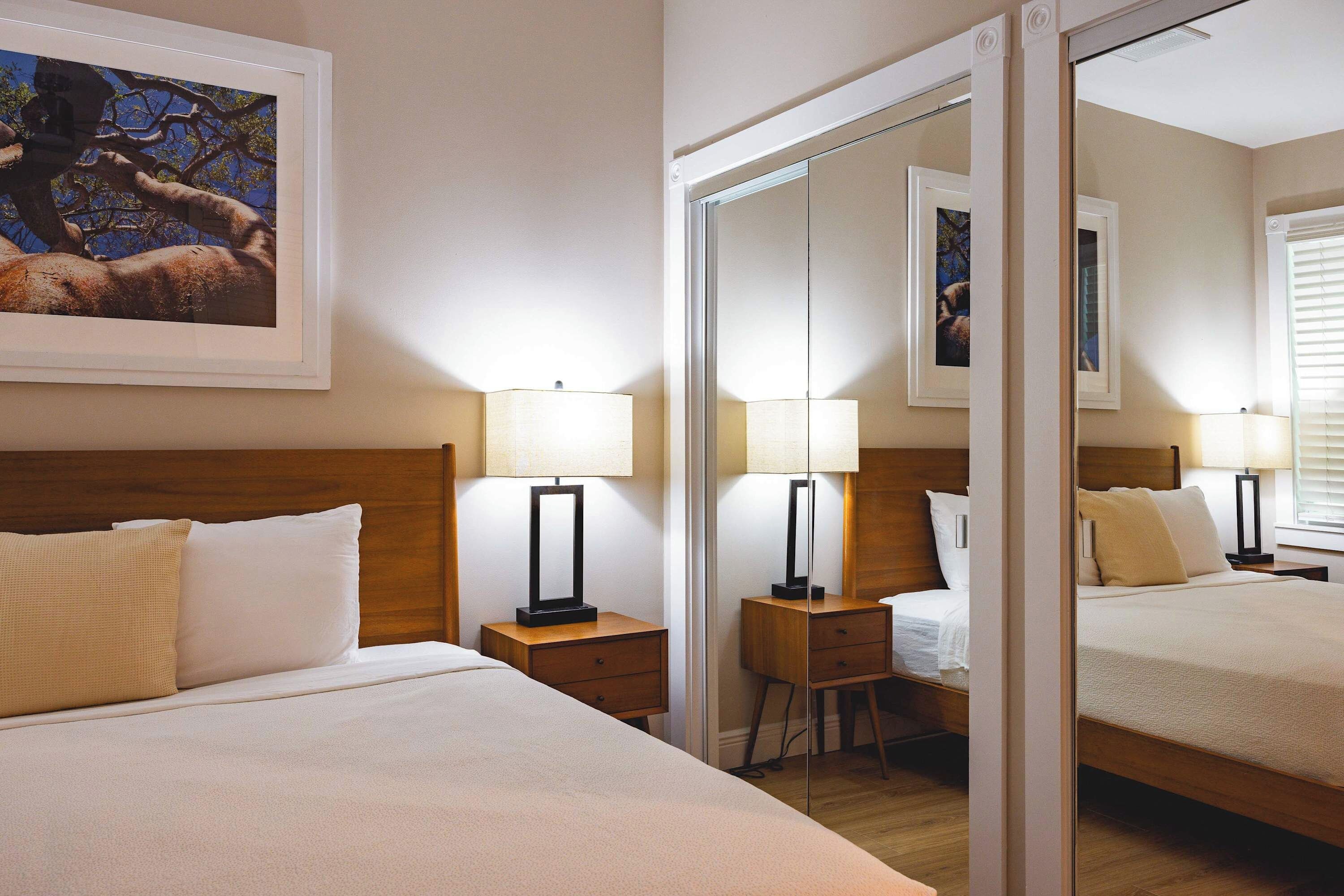 Quarto de hotel com uma cama grande, duas mesas de cabeceira com abajures, um espelho e um quadro na parede.