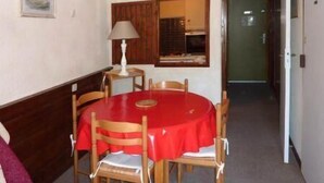 A dining area with a round table covered in a red tablecloth, wooden chairs, a lamp, and a framed picture on the wall. - Resort center, 9th floor, balcony, tv, ski locker, 32m², Les Orres (Les Orres)