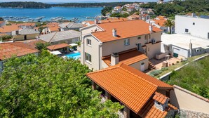 A coastal residential area with houses featuring red-tiled roofs, a swimming pool, and a marina in the background. - JURIĆ apartments with outdoor pool and bargain in RAB-PALIT (Palit)