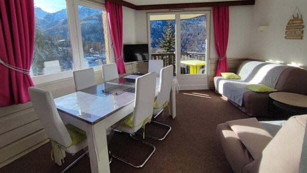 A modern room with a dining table and chairs, a sofa, and a TV. Large windows offer a mountain view. - Ski-in/ski-out & foot of the slopes, 1st floor, balcony, tv, ski locker, 38m², Les Orres (Les Orres)