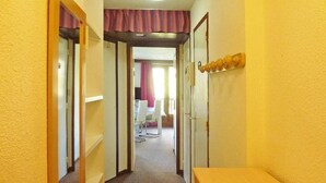 A narrow hallway with a wooden bench on the right, a door with a mirror on the left, and a room visible in the background with a bed and a window. - Ski-in/ski-out & foot of the slopes, 1st floor, balcony, tv, ski locker, 38m², Les Orres (Les Orres)