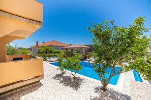 A residential area with a swimming pool, a tiled deck, and a building with a red-tiled roof. - Apt Lemon - Beautiful house in green with outdoor pool and barbecue area (Palit)