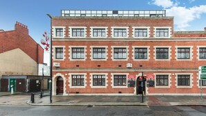 A multi-story brick building with a flat roof, large windows, and a green signboard. - Newly Refurbished 1 Bedroom Whitechapel (London)