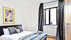 A bedroom with a bed, a window with curtains, a radiator, and a framed picture on the wall. - Newly Refurbished 1 Bedroom Whitechapel (London)