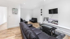 A modern living room with a black leather sofa, a coffee table, and a flat-screen TV mounted on the wall. - Newly Refurbished 1 Bedroom Whitechapel (London)